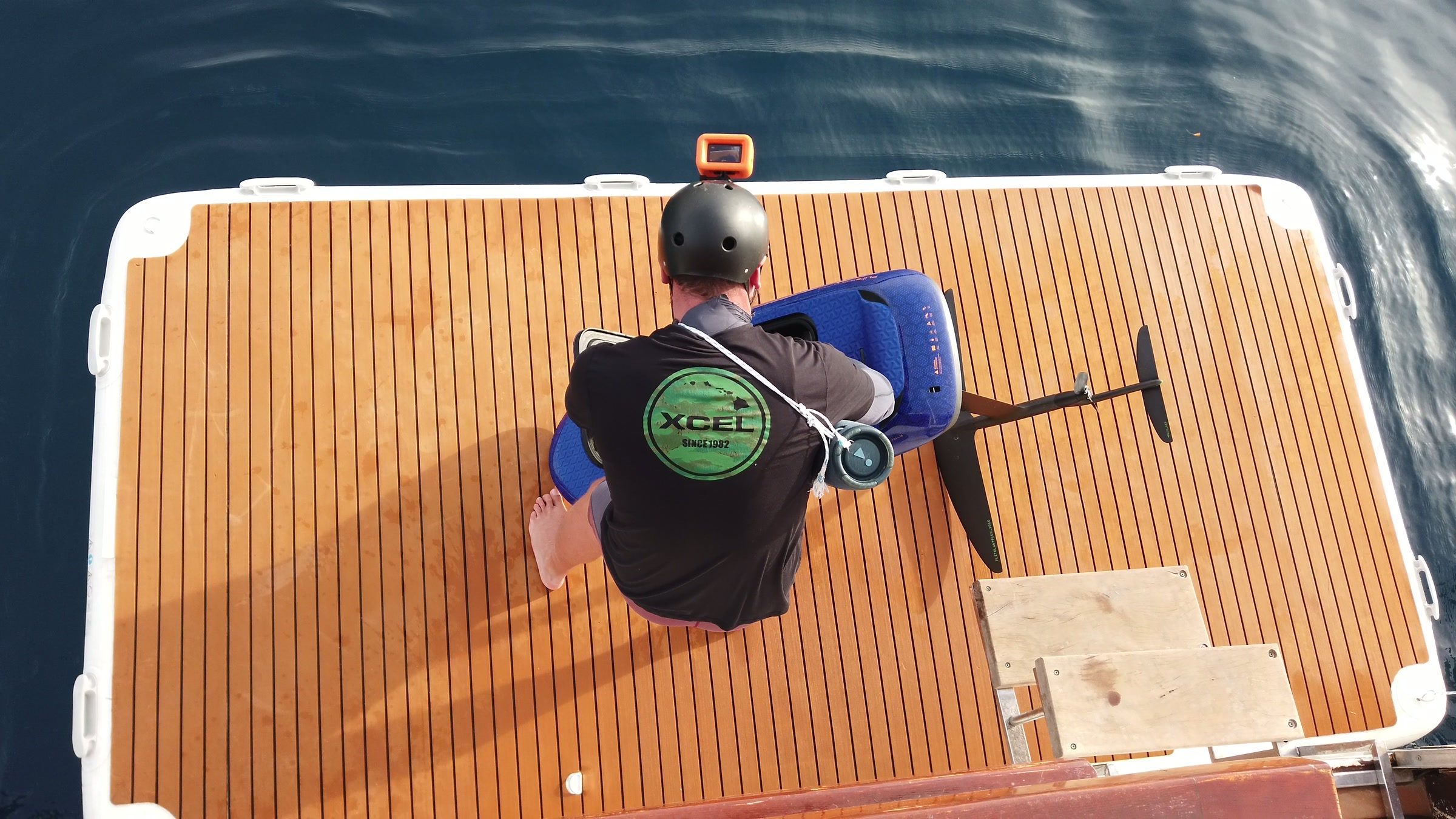 Seen from above, a rider in a helmet prepares the eFoil board and wing on the swim platform.