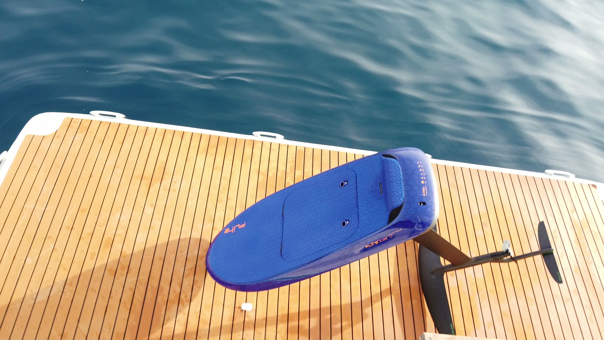 An eFoil board and its hydrofoil wing lying on a teak swim platform above the sea.