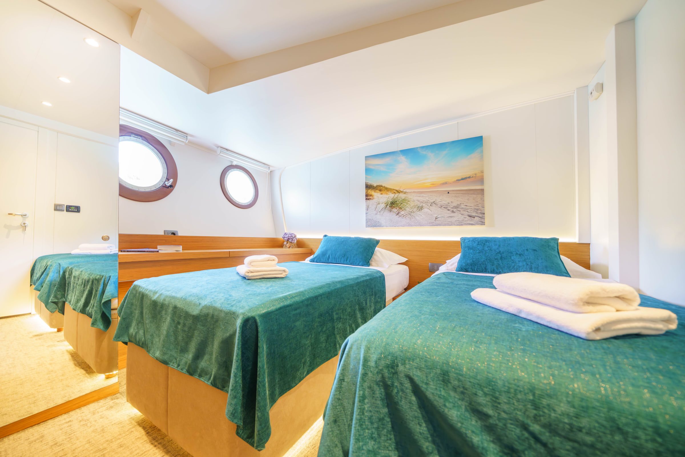 A twin cabin with two beds, fresh towels and round portholes.