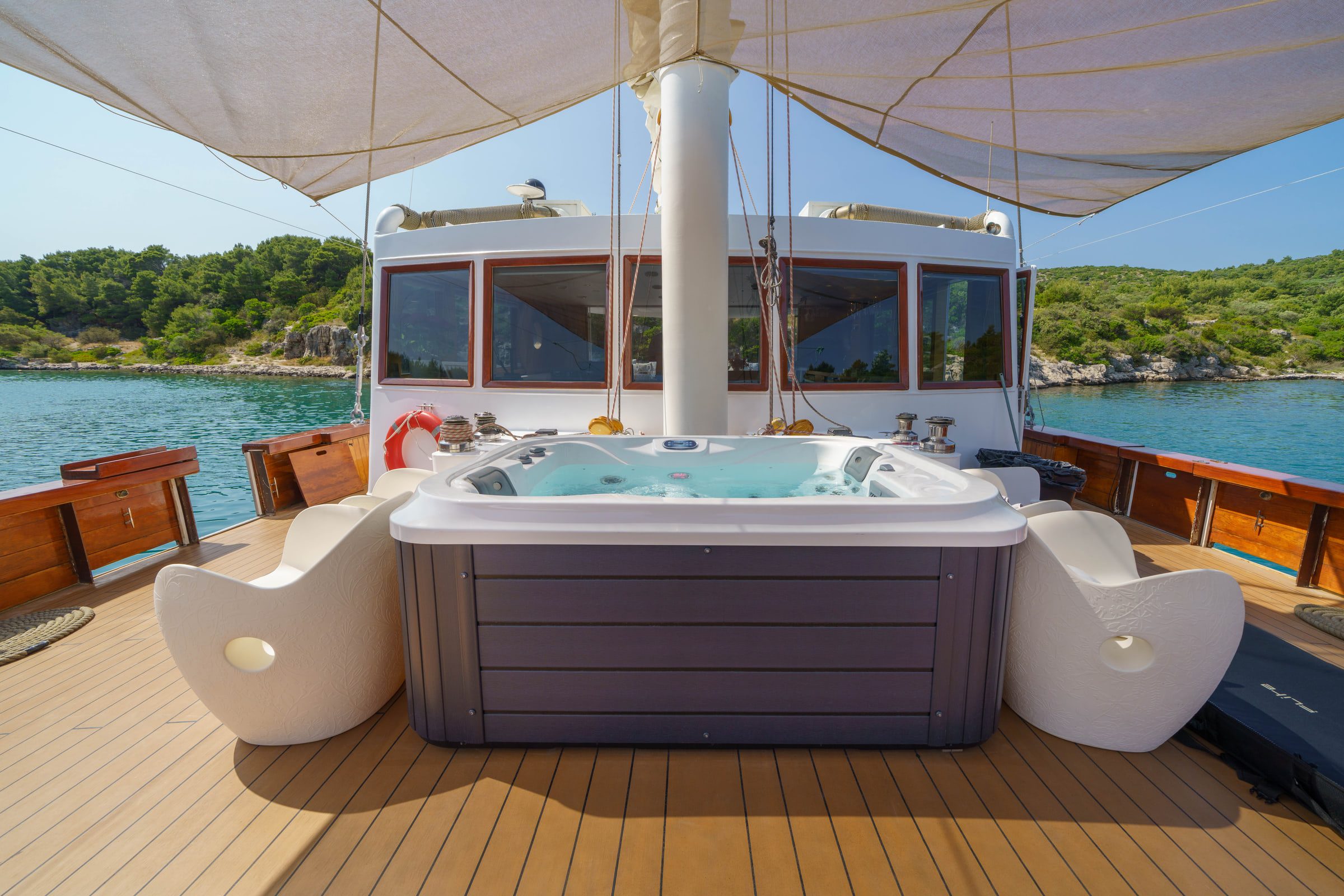 A hot tub on the teak deck in front of the wheelhouse, with lounge chairs on either side.