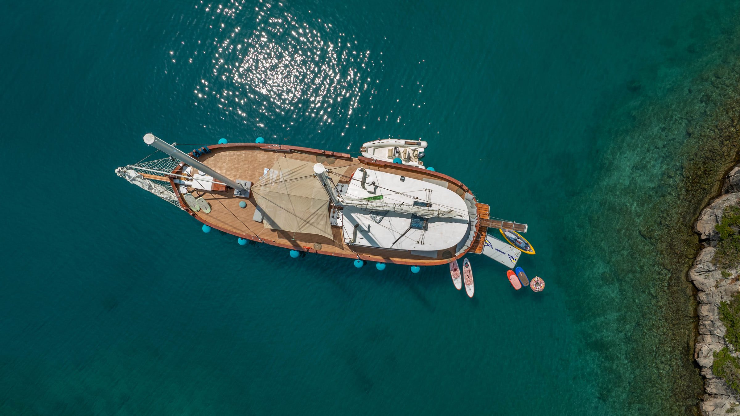 Straight from above, the Green Ray at anchor on emerald water, paddle boards trailing from the stern.