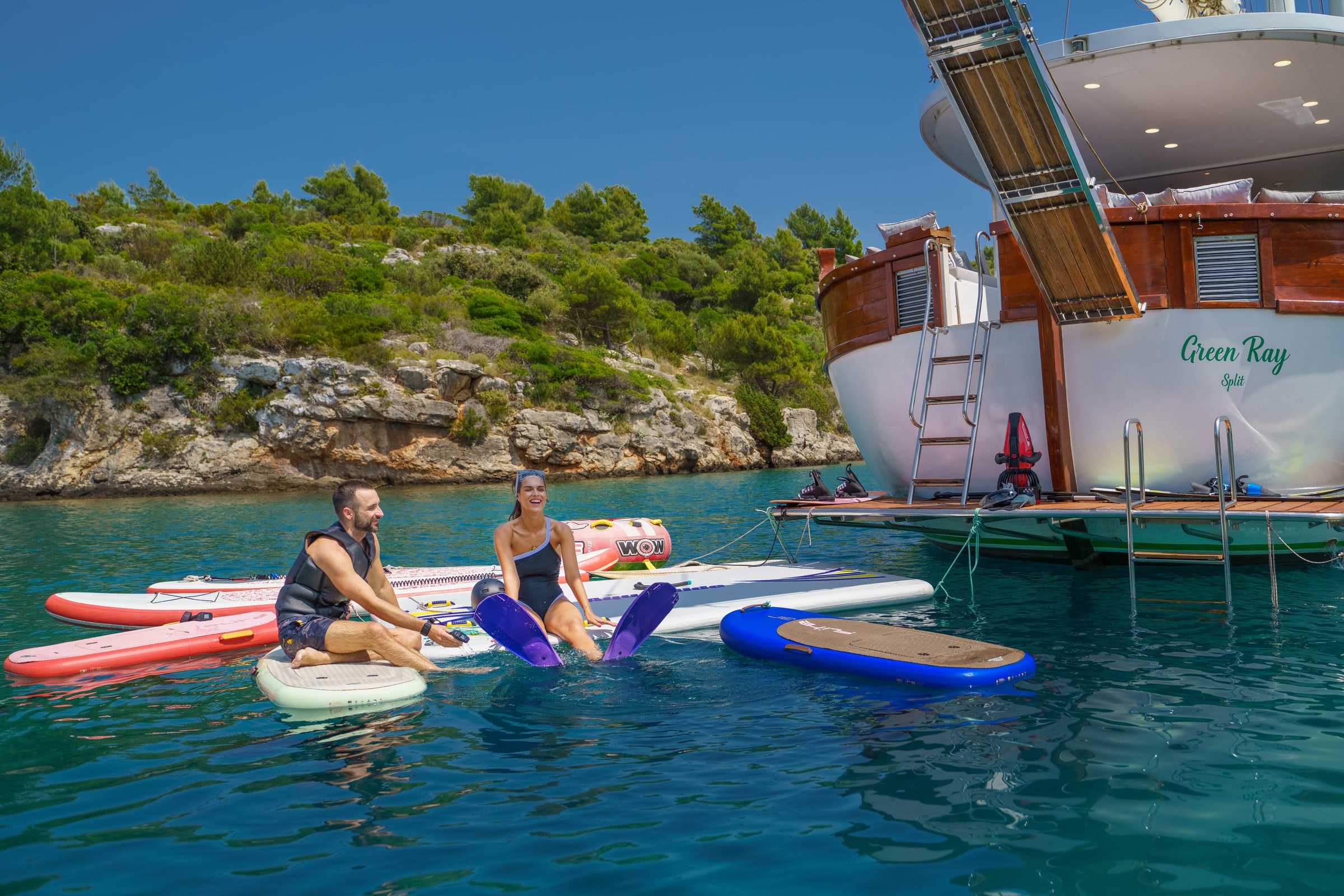 Guests relax on paddle boards and a floating mat beside the Green Ray's swim platform.
