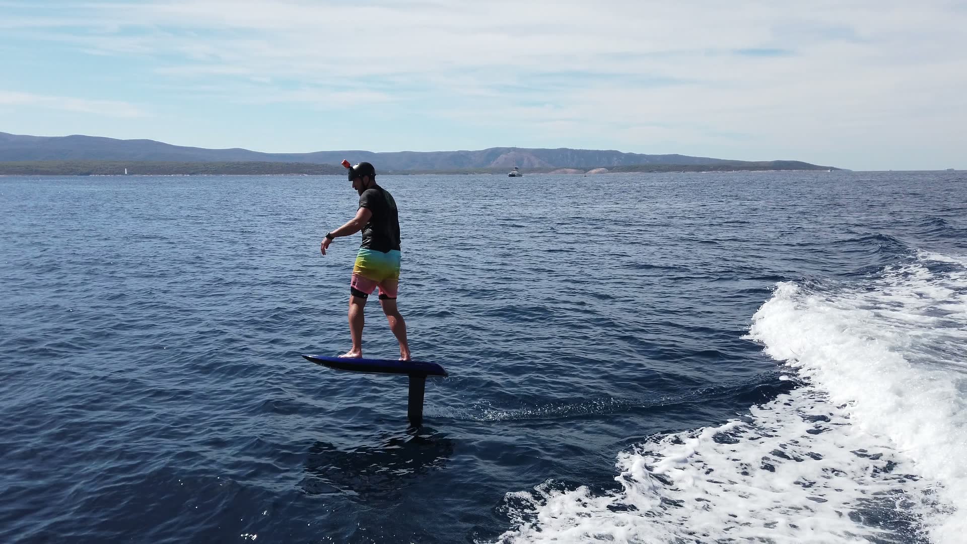 A rider in a helmet glides on an eFoil just above calm, clear Adriatic water.